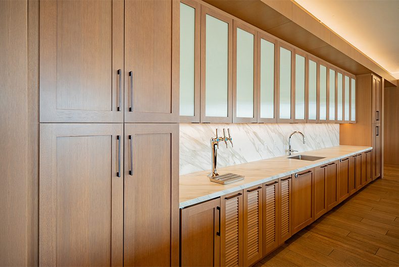 Wet bar with marble countertops, unique walnut wood cabinetry and frosted glass doors.