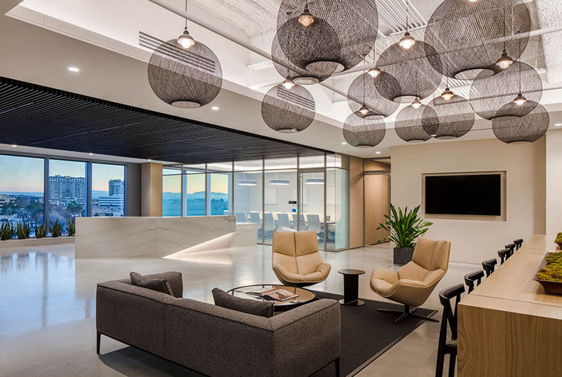 Office sitting lounge with bi-level ceilings, wall partitions and long wood table.