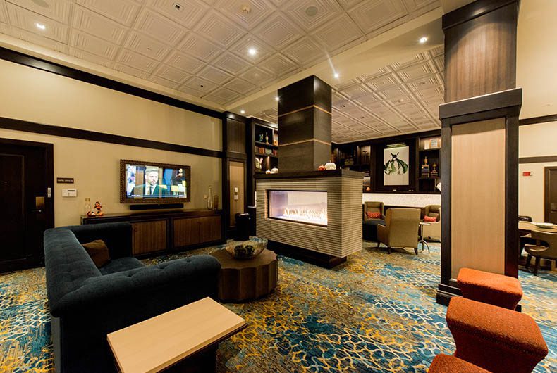 Hotel lounge sitting area with decorative tiled ceiling, wood paneled columns, entertainment center and seating