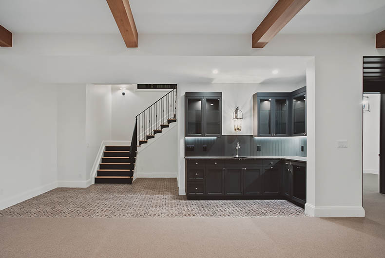 Refurnished basement with custom wood stairs and railings, wood ceiling beams and wet bar with built-in cabinetry